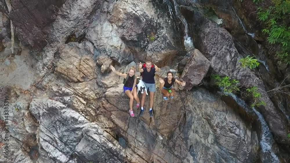 Young Tourists Resting at the Cascade Waterfall and Waving Their Hands in the Camera. HD Aerial Slowmotion. Thailand. Young Tourists Resting at the Cascade Waterfall and Waving Their Hands in the Camera. HD Aerial Slowmotion. Thailand.