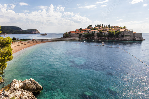 Sand beach with wooden chairs and umbrellas near the Sveti Stefan historical town on the island.