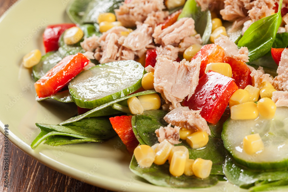 Fresh spinach salad with tuna, cucumber, corn, and red paprika on a plate Fresh spinach salad with tuna, cucumber, corn, and red paprika on a plate