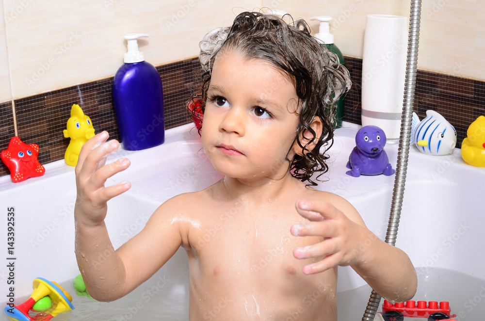Beautiful toddler taking a bath in a bathtub with bubbles. Cute kid washing his hair with