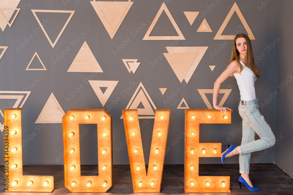 Φωτογραφία A girl in white singlet and blue denim with holes leaning on a wooden lettering