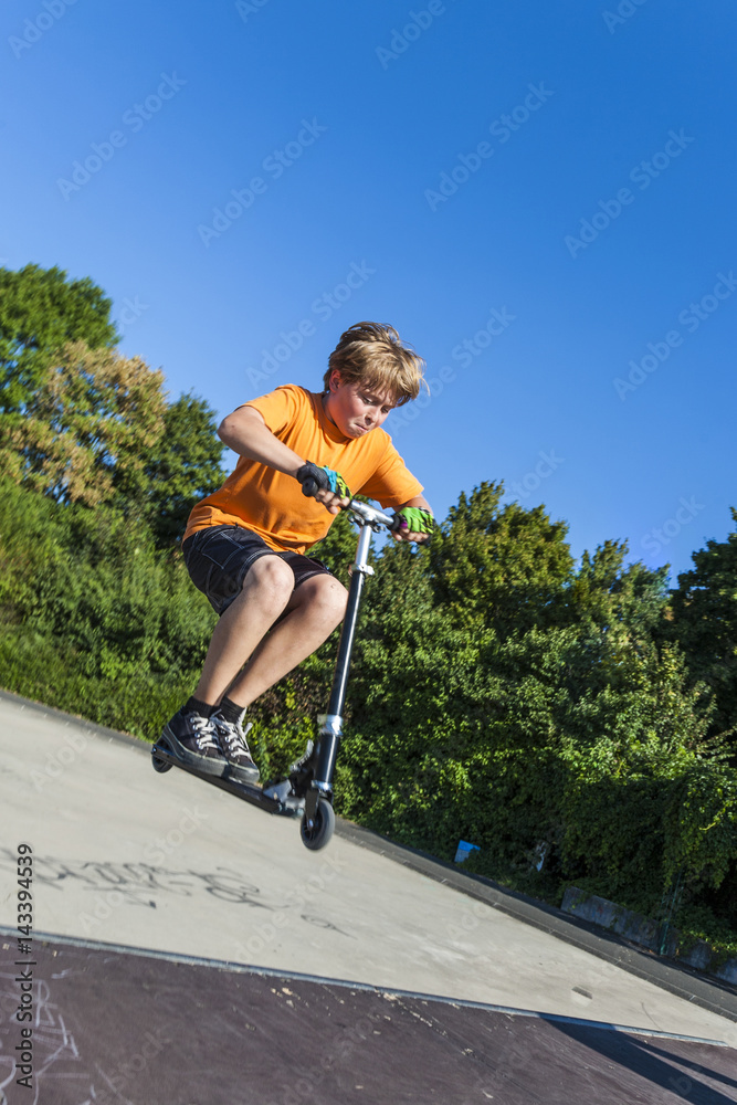 boy has fun riding push scooter at the skate park