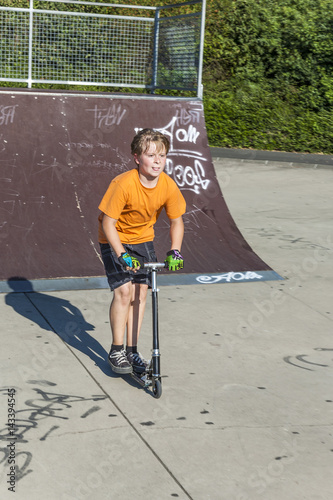 boy has fun riding push scooter at the skate park