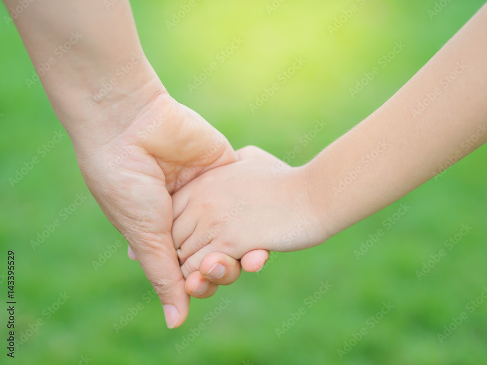 Mother holding a hand of her kid in spring day outdoors with green field background Mother holding a hand of her kid in spring day outdoors with green field background
