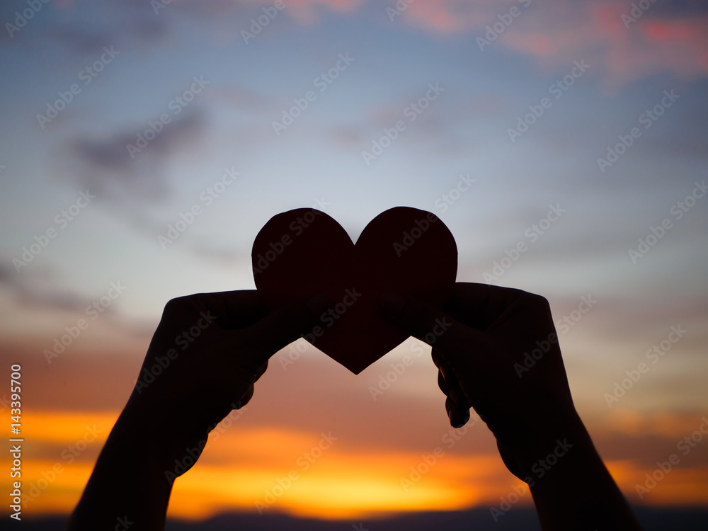 silhouette hand is raising the red paper heart with blur sunlight during sunset, Valentines day