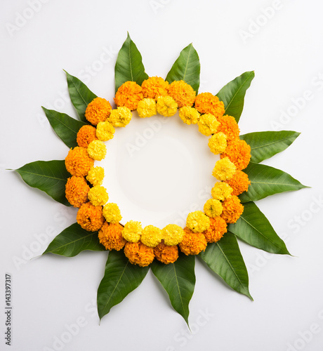 Fototapeta Naklejka Na Ścianę i Meble -  flower rangoli made using marigold or zendu flowers and mango leaves over plain background with copy space in the middle, selective focus