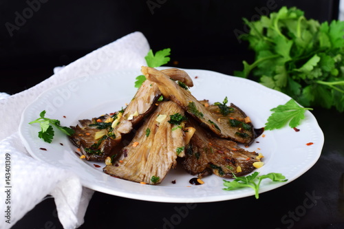 Fried oyster mushrooms with garlic, parsley in a balsamic glaze on a black background. Healthy eating concept.