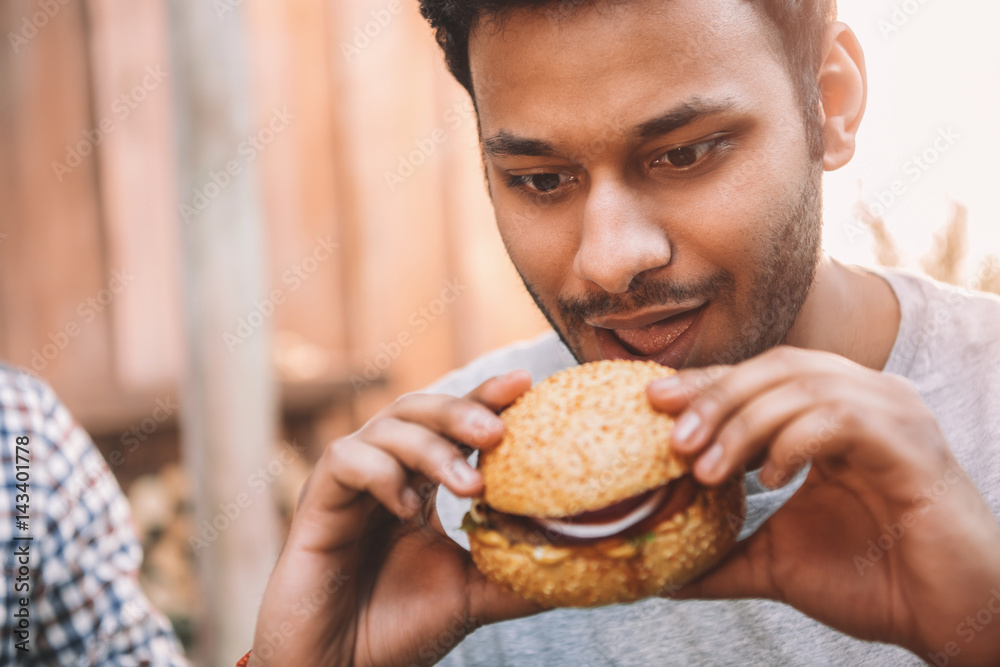 Hungry young man holding and looking at fresh tasty hamburger Hungry young man holding and looking at fresh tasty hamburger