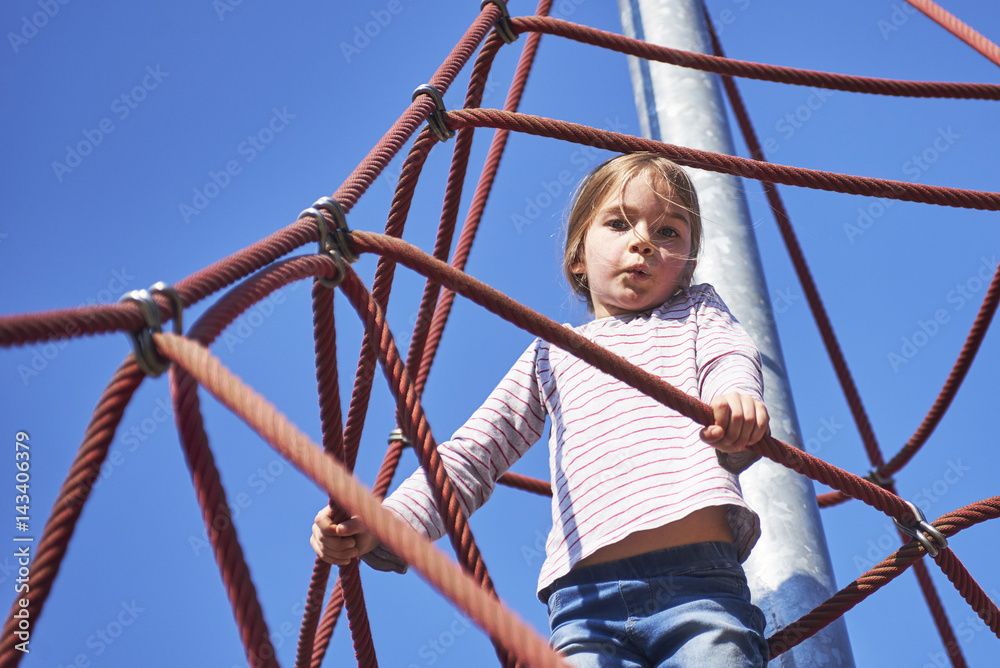 Active young child girl climbing the spider web playground activity. Children summer activities.