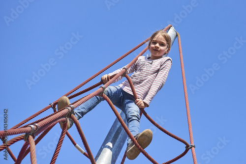 Active young child girl climbing the spider web playground activity. Children summer activities.