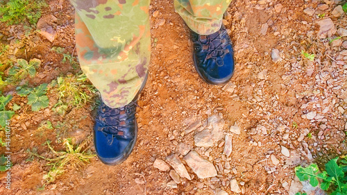 Close up of tourist or hunter legs in hiking boots and camo trousers standing on stone path.