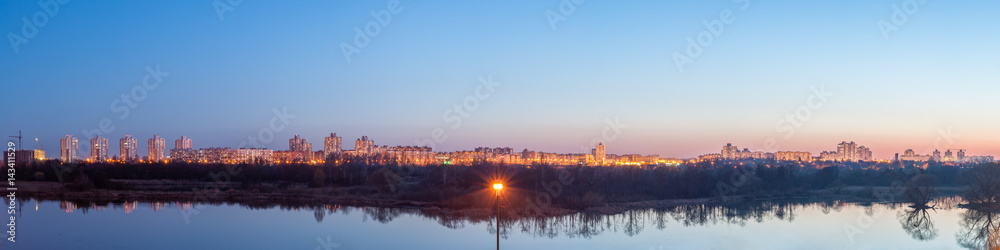 Evening panoramic cityscape. The residential quarter behind the lake is illuminated by street lights and light from the windows