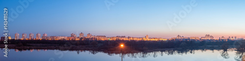 Fototapeta Naklejka Na Ścianę i Meble -  Evening panoramic cityscape. The residential quarter behind the lake is illuminated by street lights and light from the windows