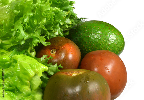 Freshly washed vegetables to prepare a green salad: ripe avocado, three black tomatoes 