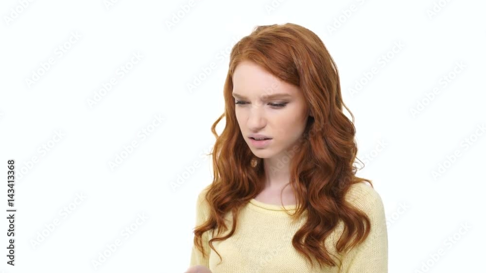 Young displeased annoyed woman with long red hair typing message on smartphone over white background Young displeased annoyed woman with long red hair typing message on smartphone over white background