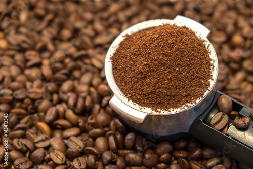 Professional metal holder with freshly ground coffee on coffee beans background
