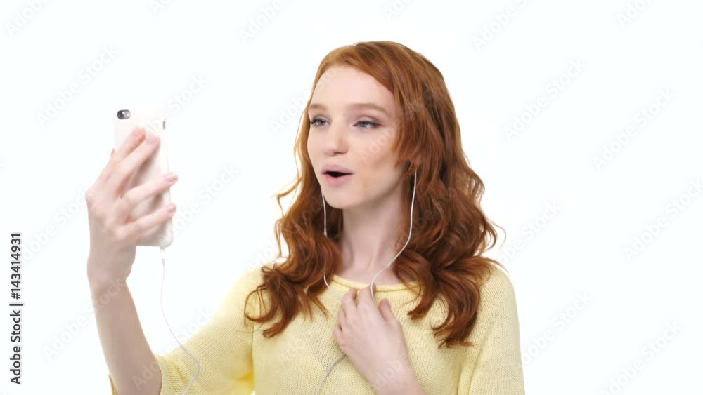 Young smiling pretty girl with long red hair having a video call with her friend on her smartphone isolated over white Young smiling pretty girl with long red hair having a video call with her friend on her smartphone isolated over white