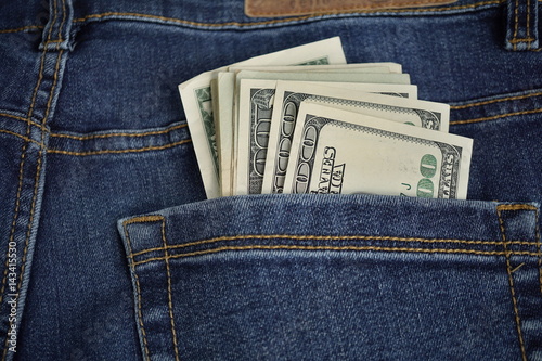 Heap of American money (US currency, USD) in the back pocket of blue jeans with yellow stitching as a symbol of black money earned without taxation 