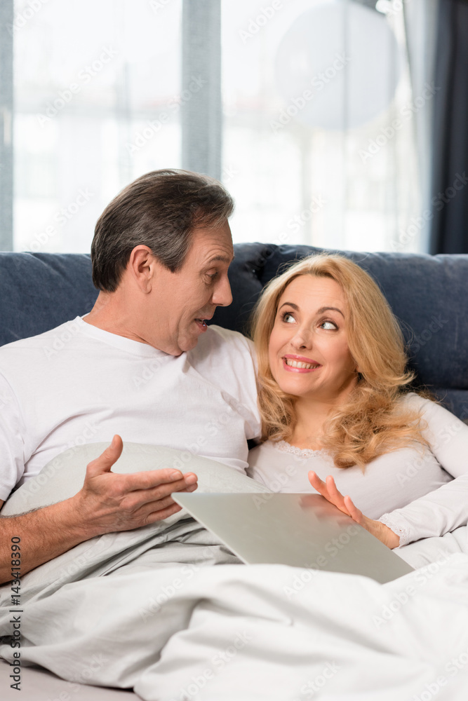 Happy middle aged couple using laptop and lying on bed at home Happy middle aged couple using laptop and lying on bed at home
