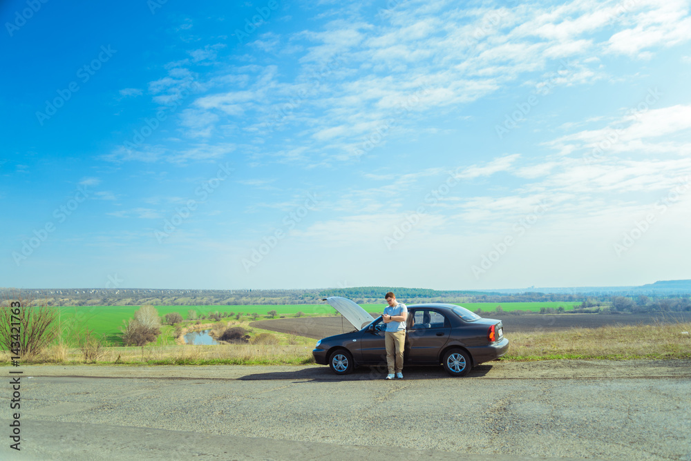 Angry young man waiting a help while sitting near the broken car Angry young man waiting a help while sitting near the broken car