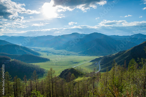 A beautiful mountain landscape. Gorgeous green valley and the beautiful hills illuminated by the sun, in the valley is a winding road. Blue sky and clouds. Journey to the Altai mountains, Russia