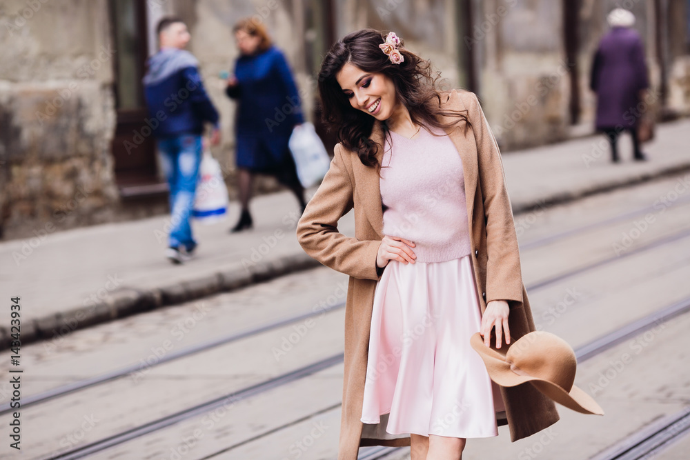 Woman in pink dress and beige coat poses on tramways