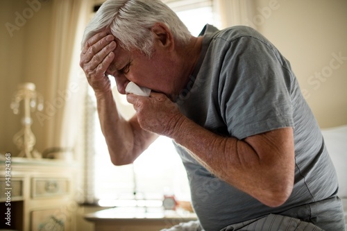 Senior man using a tissue to blow his nose in the bedroom