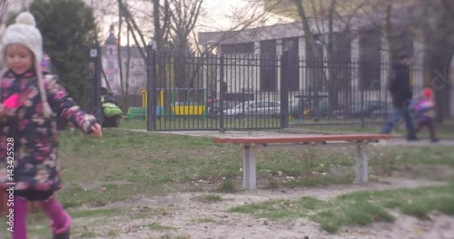 Playground With Sand and a Little Girl in a White Knitted Hat and Colored Waiscoat Entertaing There Not Far From a House in Autumn photo