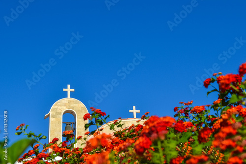 Orthodox church with a tiled roof and a bell. Red roses in the foreground. Cyprus. Ayianapa. Church of St. Epiphany. photo