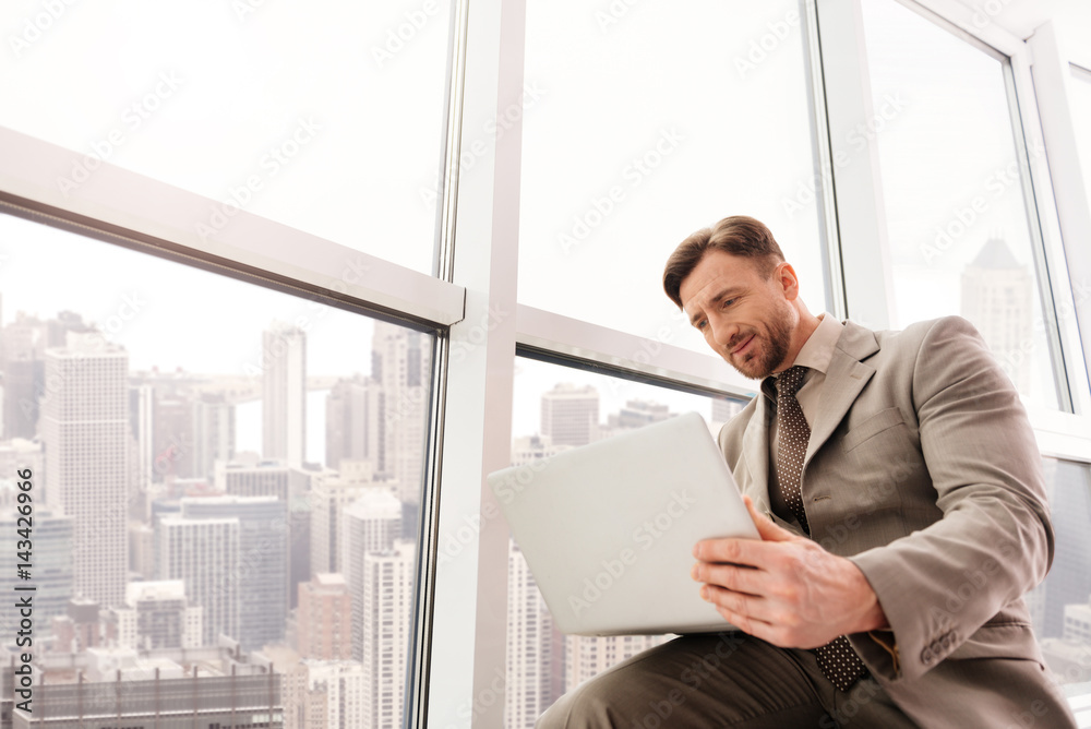 Fototapeta premium Low angle of serious businessman using laptop