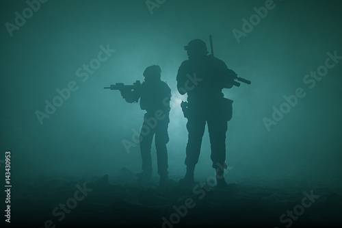 Black silhouettes of pair of soldiers in the smoke haze moving in battle operation. Back light © Getmilitaryphotos