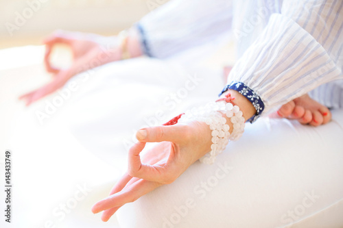 Hands of woman in meditation in a yoga posture in lotus and white malas in semi-precious stones