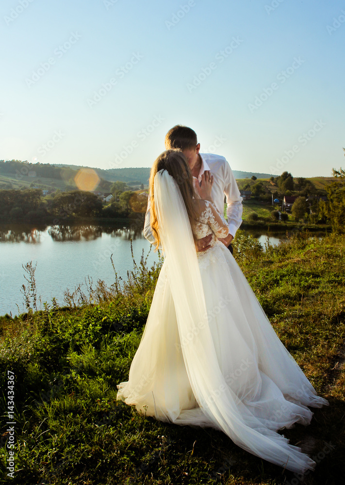 Bride and groom kissing in the sunny summer day near lake. Beauty sunlight at the outdoor in happy wedding day