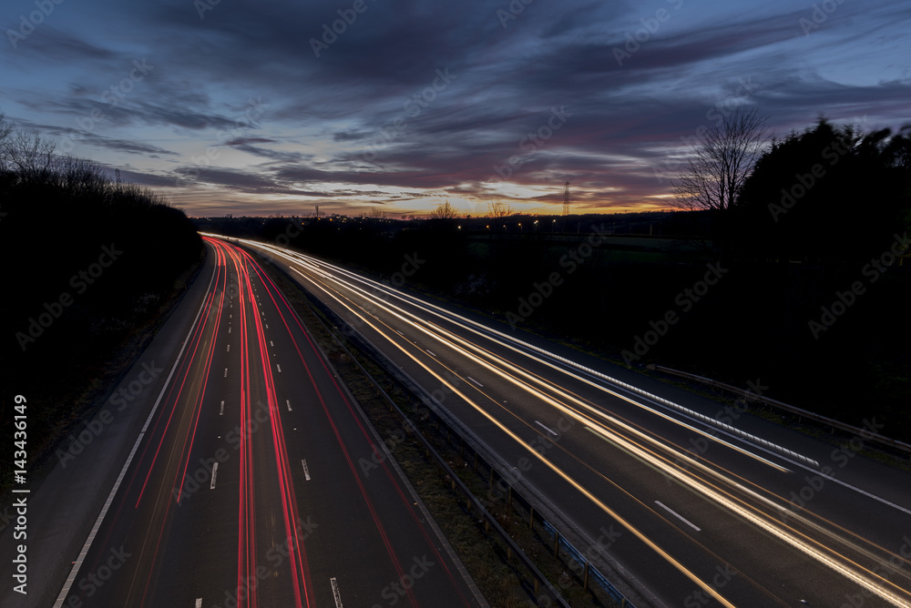 A UK motorway, at sunset, with light trails created by the traffic on the road