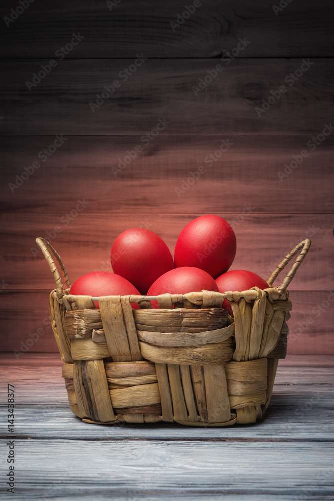 Painted Easter eggs in basket over wooden background
