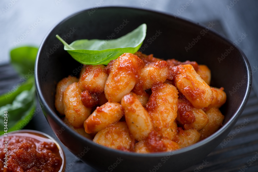 Close-up of potato gnocchi served with red pesto sauce and fresh basil in a black bowl Close-up of potato gnocchi served with red pesto sauce and fresh basil in a black bowl