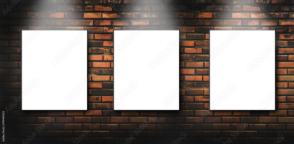 Three blank white canvas frames hang on brick wall with Light