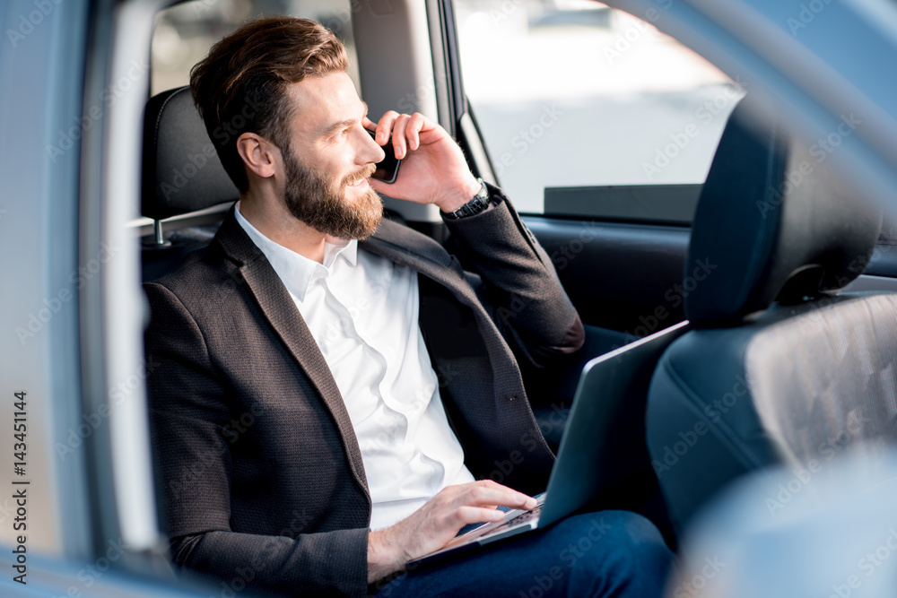 Handsome businessman talking with phone sitting on the backseat of the car