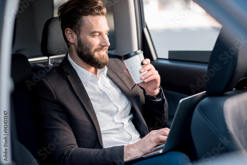 Handsome businessman sitting with coffee to go on the backseat of the car © rh2010