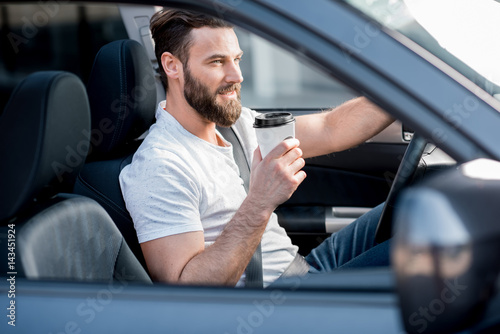 Handsome man dressed cassual in white t-shirt driving a car with coffee to go © rh2010