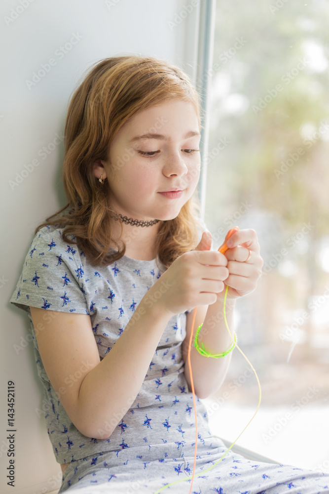 Girl sitting on the windowsill and weaves bracelet Girl sitting on the windowsill and weaves bracelet