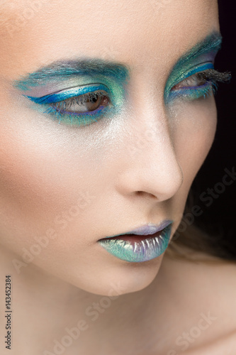 All blue. Vertical cropped closeup of a fashion model with blue and green eye shadow and metallic lipstick looking away