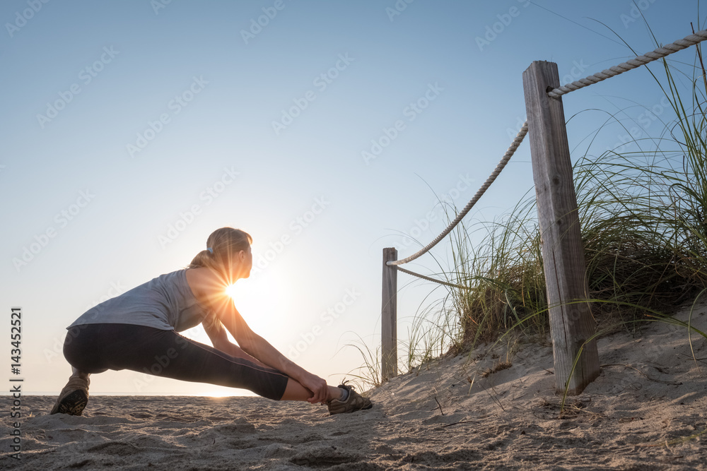Woman performs stretching exercises on a beach at sunrise Woman performs stretching exercises on a beach at sunrise