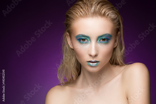 Life in color. Beautiful blonde female model looking to the camera seriously wearing professional creative makeup with blue eye shadow and metallic chameleon lips