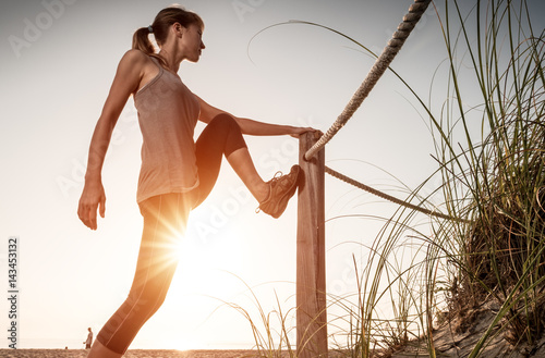 Woman performs stretching exercises on a beach at sunrise