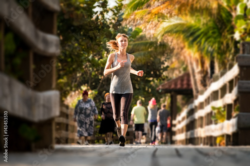 Slim young woman running on the wooden walkway in the park