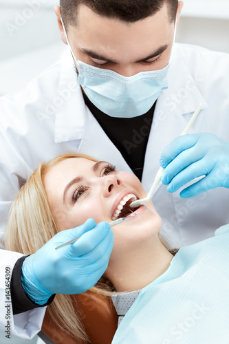 Working on her smile. Vertical closeup of a professional dentist examining teeth of a beautiful happy smiling blonde woman