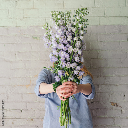 Stampa su tela Young woman holds a bunch of delphinium flowers against an old brick wall