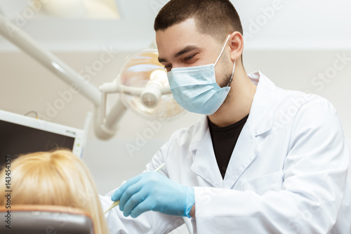 Caring for his clients. Shot of a cheerful male dentist wearing surgical mask working examining teeth of his client