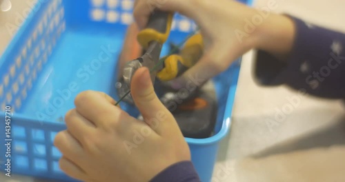 Child`s Hands Use Nippers to Cut Some Wire and Put Them Into a Basket For Tools With Pliers and Something Else Indoors photo